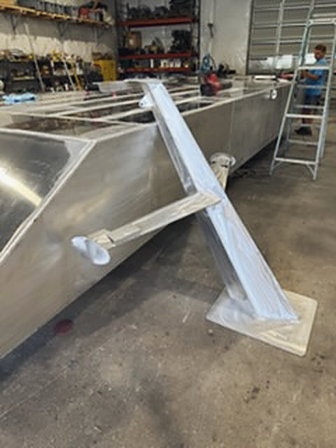 A mast on its base plate, leaning on a hull in the shop