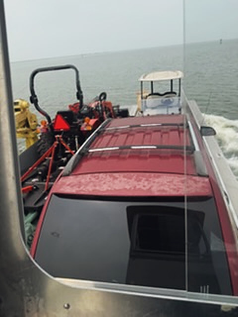 A car, a tractor and a golf cart riding across the water on a deck