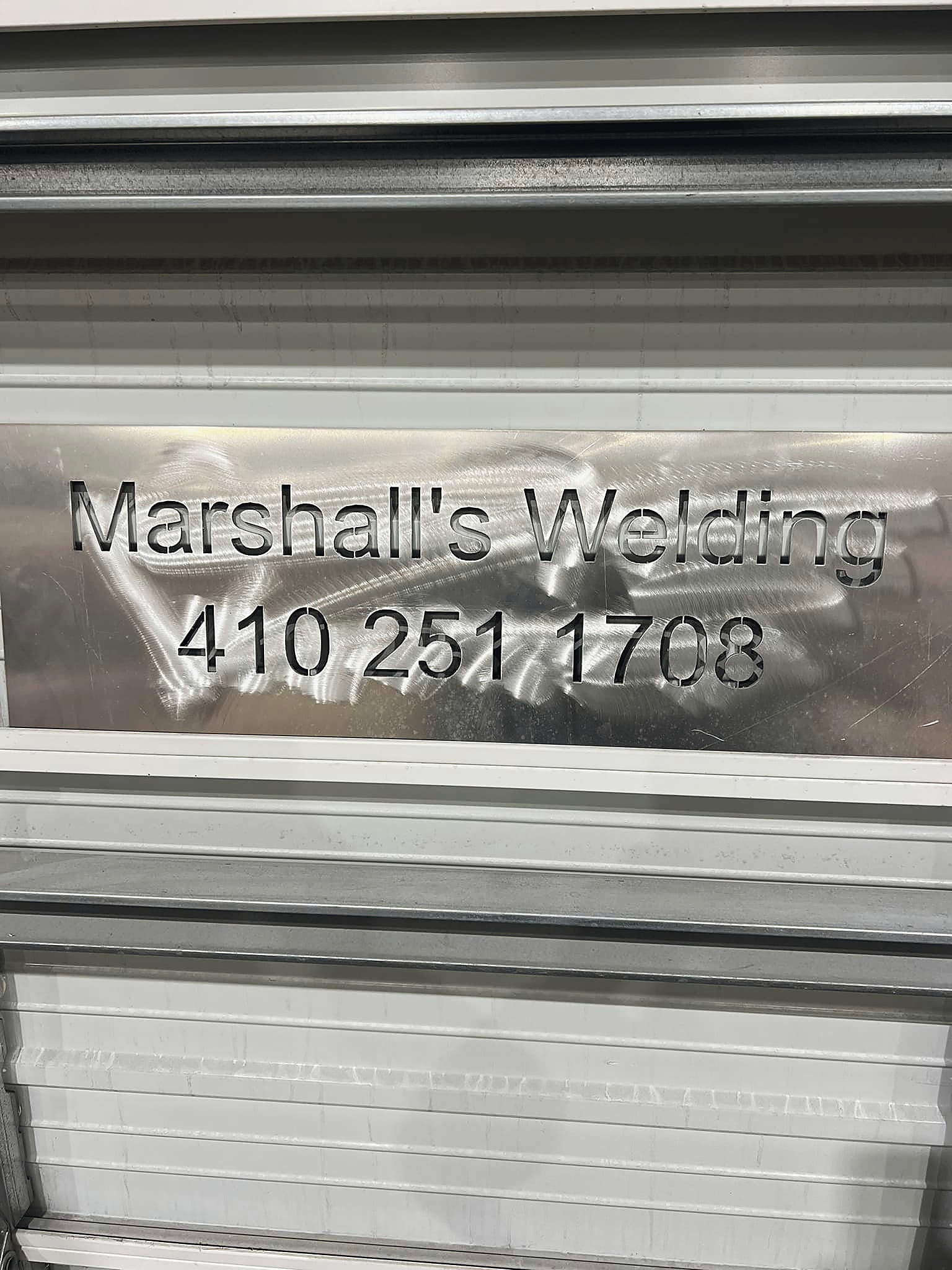 The shop name and number cut into an aluminum panel