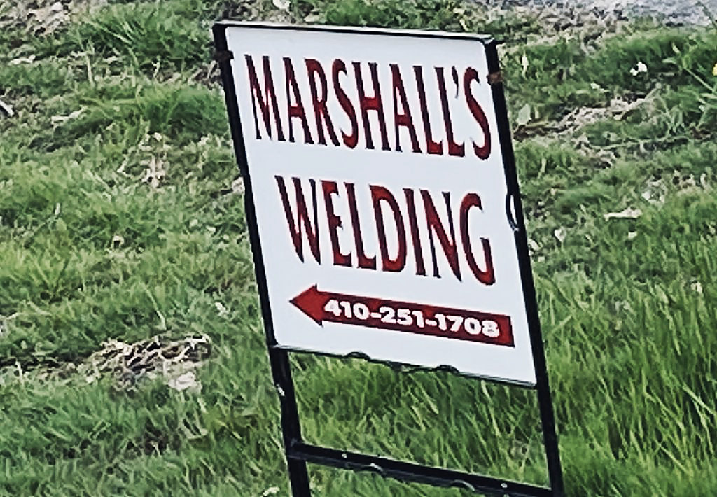 The red and white Marshall’s Welding sign out on the road, an arrow and the shop number on it